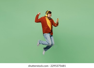 Full body side view elderly man 40s years old wears casual clothes red shirt t-shirt listen music in headphones do winner gesture use mobile cell phone isolated on plain pastel light green background - Powered by Shutterstock