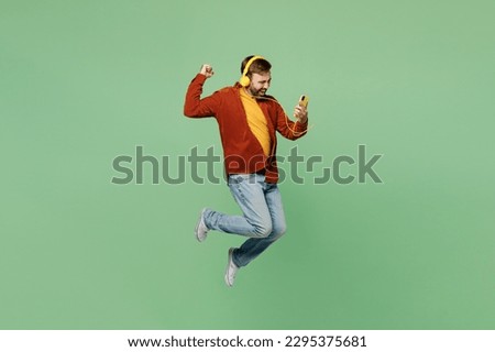 Full body side view elderly man 40s years old wears casual clothes red shirt t-shirt listen music in headphones do winner gesture use mobile cell phone isolated on plain pastel light green background