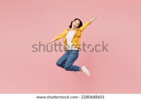 Full body side view excited young woman of Asian ethnicity wear yellow shirt white t-shirt jump high with outstretched hands look camera isolated on plain pastel light pink background studio portrait