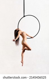 Full Body Side View Of Flexible Female Gymnast Doing Walking Pose On Aerial Hoop Against White Background In Light Studio