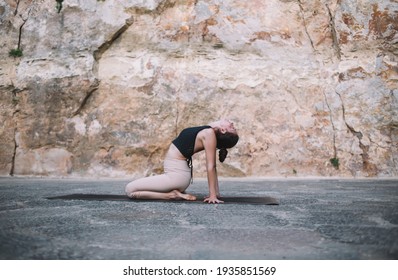 Full body side view of focused female bending back while sitting on legs and leaning on hands with head thrown back