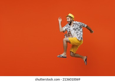 Full body side view fun excited young tourist man wear beach shirt hat jump high run fast hurry up isolated on plain orange color background studio portrait. Summer vacation sea rest sun tan concept