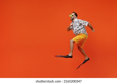 Full body side view fun young tourist man in beach shirt goggles flippers run fast jump travel abroad on weekends isolated on plain orange background studio Summer vacation sea rest sun tan concept