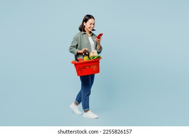 Full body side view fun young woman wear casual clothes hold red basket with food products use mobile phone isolated on plain blue background studio portrait. Delivery service from shop or restaurant - Powered by Shutterstock