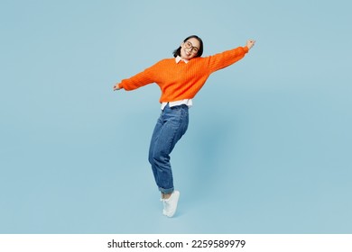 Full body side view fun young woman of Asian ethnicity wear orange sweater glasses stand on toes leaning back with outstretched hands dance isolated on plain pastel light blue cyan background studio - Powered by Shutterstock