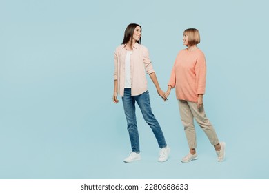 Full body side view fun elder parent mom with young adult daughter two women together wearing casual clothes hold hands walk go look to each other isolated on plain blue background. Family day concept - Shutterstock ID 2280688633