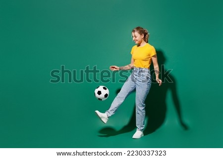 Full body side view fun active young woman fan wear basic yellow t-shirt cheer up support football sport team kick soccer ball on foot leg watch tv live stream isolated on dark green background studio