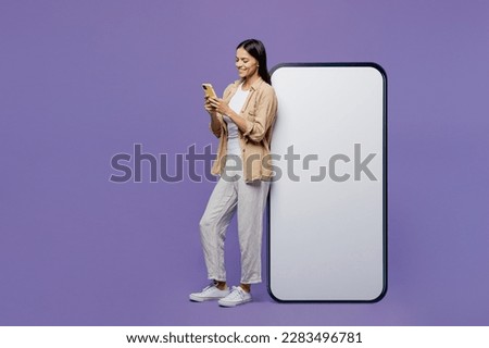 Full body side view fun young latin woman wear light shirt casual clothes big huge blank screen mobile cell phone smartphone with area hold use device isolated on plain pastel purple color background