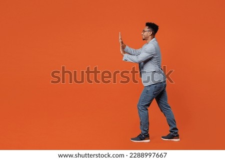 Full body side view fun young employee business man corporate lawyer wear classic formal grey suit shirt glasses work in office push something invisible isolated on plain red orange background studio
