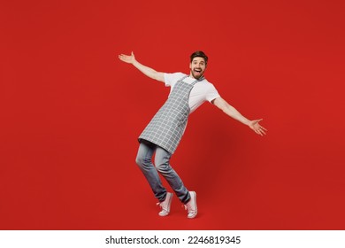 Full body side view happy young housekeeper chef cook baker man wear grey apron look camera with outstretched hands stand on toes lean back isolated on plain red background studio Cooking food concept - Powered by Shutterstock