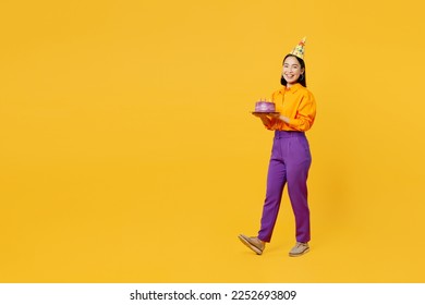 Full body side view happy smiling fun young woman wears casual clothes hat celebrating hold in hand cake with candles walk go isolated on plain yellow background. Birthday 8 14 holiday party concept