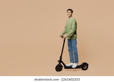 Full body side view happy fun young man of African American ethnicity wear green sweatshirt riding e-scooter isolated on plain pastel light beige background studio portrait. People lifestyle concept - Powered by Shutterstock