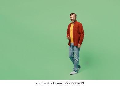 Full body side view happy smiling elderly man 40s years old wears casual clothes red shirt t-shirt walking going strolling look camera isolated on plain pastel light green background studio portrait