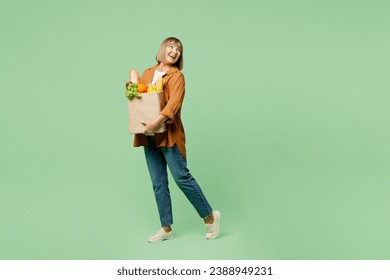 Full body side view happy elderly woman wears brown shirt casual clothes hold shopping paper bag with food products look aside on area isolated on plain green background. Delivery service from shop - Powered by Shutterstock