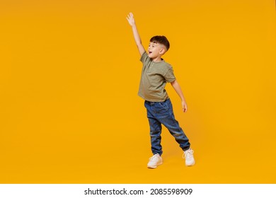 Full body side view little small smiling happy boy 6-7 years old wear green t-shirt walk go waving hand isolated on plain yellow background studio portrait. Mother's Day love family lifestyle concept