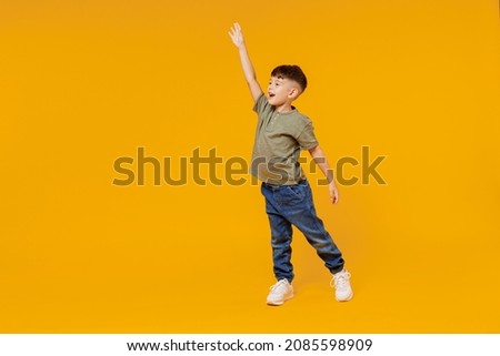 Full body side view little small smiling happy boy 6-7 years old wear green t-shirt walk go waving hand isolated on plain yellow background studio portrait. Mother's Day love family lifestyle concept