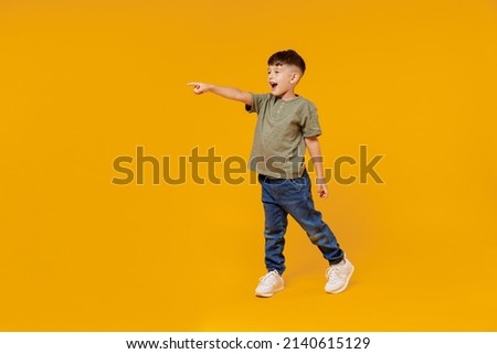 Full body side view little small smiling happy boy 6-7 years old wearing green t-shirt walk go point finger aside on area isolated on plain yellow background Mother's Day love family lifestyle concept