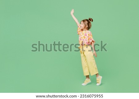 Full body side view little child kid girl 6-7 years old wear casual clothes raise up waving hand isolated on plain pastel green background studio portrait. Mother's Day love family lifestyle concept