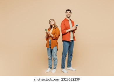 Full body side view minded young couple two friends family man woman wears casual clothes hold in hand use mobile cell phone together isolated on pastel plain beige color background studio portrait - Powered by Shutterstock