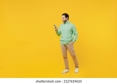 Full body side view smiling happy young man 20s wearing mint knitted sweater hold in hand use mobile cell phone isolated on plain yellow background studio portrait. People lifestyle fashion concept - Powered by Shutterstock