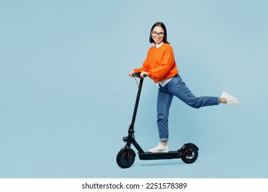 Full body side view smiling happy young woman of Asian ethnicity wear orange sweater glasses riding electric scooter isolated on plain pastel light blue cyan background studio People lifestyle concept - Powered by Shutterstock