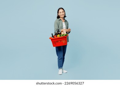 Full body side view smiling young woman wear casual clothes hold red basket with food products look camera isolated on plain blue background studio portrait. Delivery service from shop or restaurant - Powered by Shutterstock