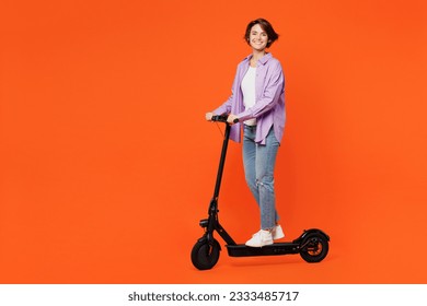 Full body side view smiling fun young woman wear purple shirt white t-shirt casual clothes riding electric scooter look camera isolated on plain orange background studio portrait. Lifestyle concept - Powered by Shutterstock