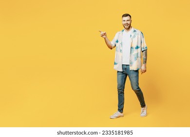 Full body side view smiling happy young man wear blue shirt white t-shirt casual clothes walk go point index finger aside on area isolated on plain yellow background studio portrait. Lifestyle concept