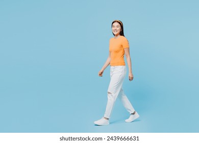 Full body side view smiling happy young woman of Asian ethnicity she wears orange t-shirt casual clothes walk go isolated on plain pastel light blue cyan background studio portrait. Lifestyle concept - Powered by Shutterstock