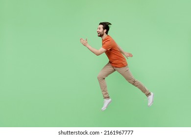 Full Body Side View Sporty Young Man 20s Wearing Casual Orange T-shirt Jumping High Run Fast Hurry Up Isolated On Plain Pastel Light Green Color Background Studio Portrait. People Lifestyle Concept