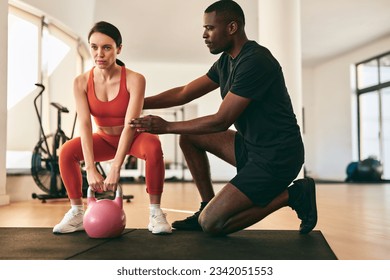 Full body side view of strong man personal trainer in sportswear instructing female client on exercise with weight lifting at gym - Powered by Shutterstock