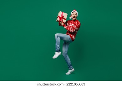 Full body side view surprised merry young man wear red warm knitted sweater Santa hat posing hold present box with gift ribbon bow isolated on plain dark green background New Year 2023 holiday concept - Powered by Shutterstock