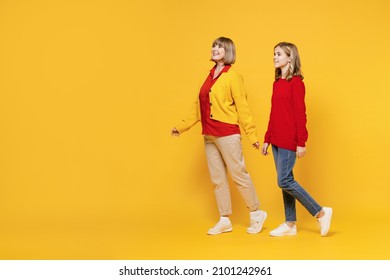 Full Body Side View Woman 50s In Red Shirt Have Fun With Teenager Girl 12-13 Years Old. Grandmother Granddaughter Walk Going Strolling Isolated On Plain Yellow Background. Family Lifestyle Concept.