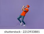 Full body side view young singer fun man 20s he wearing red hat t-shirt isolated on plain pastel light purple sing song in microphone at karaoke club leaning back background. People lifestyle concept