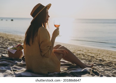 Full Body Side View Young Woman In Straw Hat Shirt Summer Clothes Sit On Plaid Have Picnic Drink Red Wine Glass Outdoors On Sea Sunrise Sand Beach Background People Vacation Lifestyle Journey Concept.