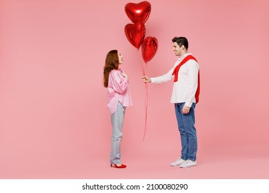Full body side view young couple two friends woman man 20s in shirt hold bunch of red inflatable balloons isolated on plain pastel pink background studio Valentine's Day birthday holiday party concept