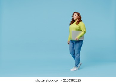 Full Body Side View Young Chubby Overweight Plus Size Big Fat Fit Woman 20s Wear Green Sweater Hold Closed Laptop Pc Computer Walking Going Isolated On Plain Blue Background. People Lifestyle Concept