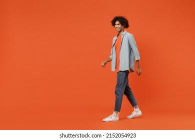 Full Body Side View Young Smiling Cheerful Black Student Man 20s Wearing Blue Shirt T-shirt Looking Aside Walk Go Isolated On Plain Orange Color Background Studio Portrait. People Lifestyle Concept.