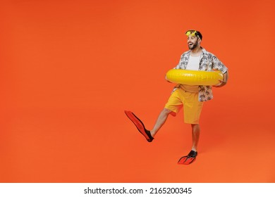 Full body side view young tourist man in beach shirt goggles hold inflatable ring flippers travel abroad on weekends isolated on plain orange background studio Summer vacation sea rest sun tan concept
