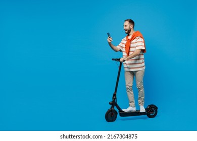 Full body side view young smiling happy cool man 20s wearing orange striped t-shirt riding electric scooter use mobile cell phone isolated on plain blue background studio. People lifestyle concept. - Powered by Shutterstock