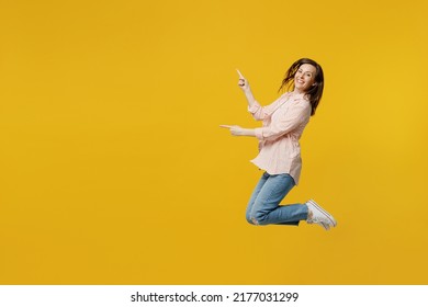 Full Body Side View Young Happy Woman She 30s Wear Striped Shirt White T-shirt Jump Hight Point Index Finger Camera On You Isolated On Plain Yellow Background Studio Portrait. People Lifestyle Concept