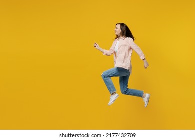 Full body side view young happy sporty fun woman she 30s wears striped shirt white t-shirt jump high run fast hurry up isolated on plain yellow background studio portrait. People lifestyle concept.