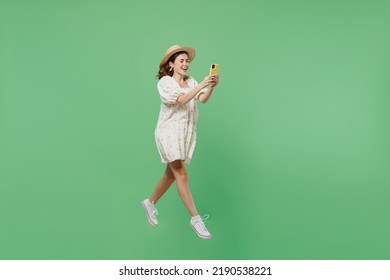 Full Body Side View Young Happy Woman She 20s Wears White Dress Hat Hold In Hand Mobile Cell Phone Jump High Isolated On Plain Pastel Light Green Background Studio Portrait. People Lifestyle Concept