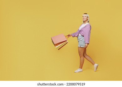 Full Body Side View Young Blonde Woman 20s Wear Pink Tied Shirt White T-shirt Holding Package Bags With Purchases After Shopping Walk Go Isolated On Plain Yellow Background People Lifestyle Concept