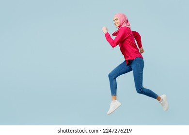 Full body side view young arabian asian muslim woman wear pink abaya hijab hurry run fast in rush jump high isolated on plain pastel light blue cyan background studio portrait People uae islam concept - Powered by Shutterstock