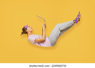 Full body side view young woman wears purple pyjamas jam sleep eye mask rest relax at home fly up hover over air fall down use laptop pc computer isolated on plain yellow background Night nap concept