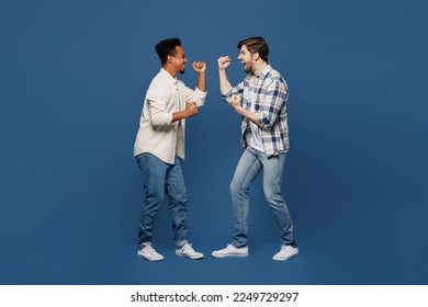 Full body side view young two friends men wear white casual shirts together do winner gesture celebrate clenching fists say yes isolated plain dark royal navy blue background. People lifestyle concept - Shutterstock ID 2249729297