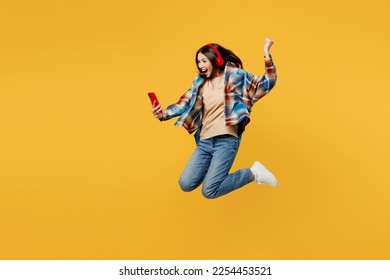 Full body side view young excited fun cheerful caucasian woman in blue shirt beige t-shirt headphones listen music use mobile cell phone jump high isolated on plain yellow background studio portrait - Shutterstock ID 2254453521