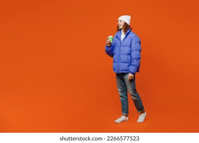 Full body side view young man with long curly hair wear hat purple ski padded jacket casual clothes hold takeaway delivery craft paper brown cup coffee to go isolated on plain orange red background - Powered by Shutterstock