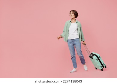Full body side view young traveler woman wear green shirt hold suitcase isolated on plain pastel light pink background Tourist travel abroad in free time rest getaway Air flight trip journey concept - Shutterstock ID 2274138043